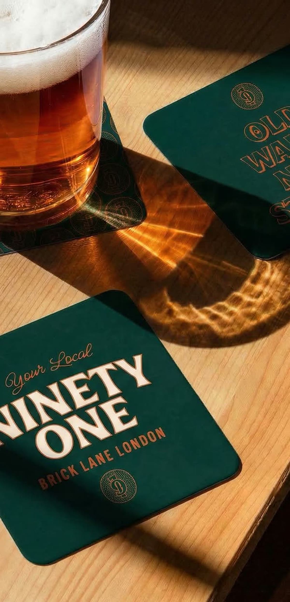 Ahşap bar tezgahında koyu yeşil kare bira bardak altlıkları ve bir bardak bira